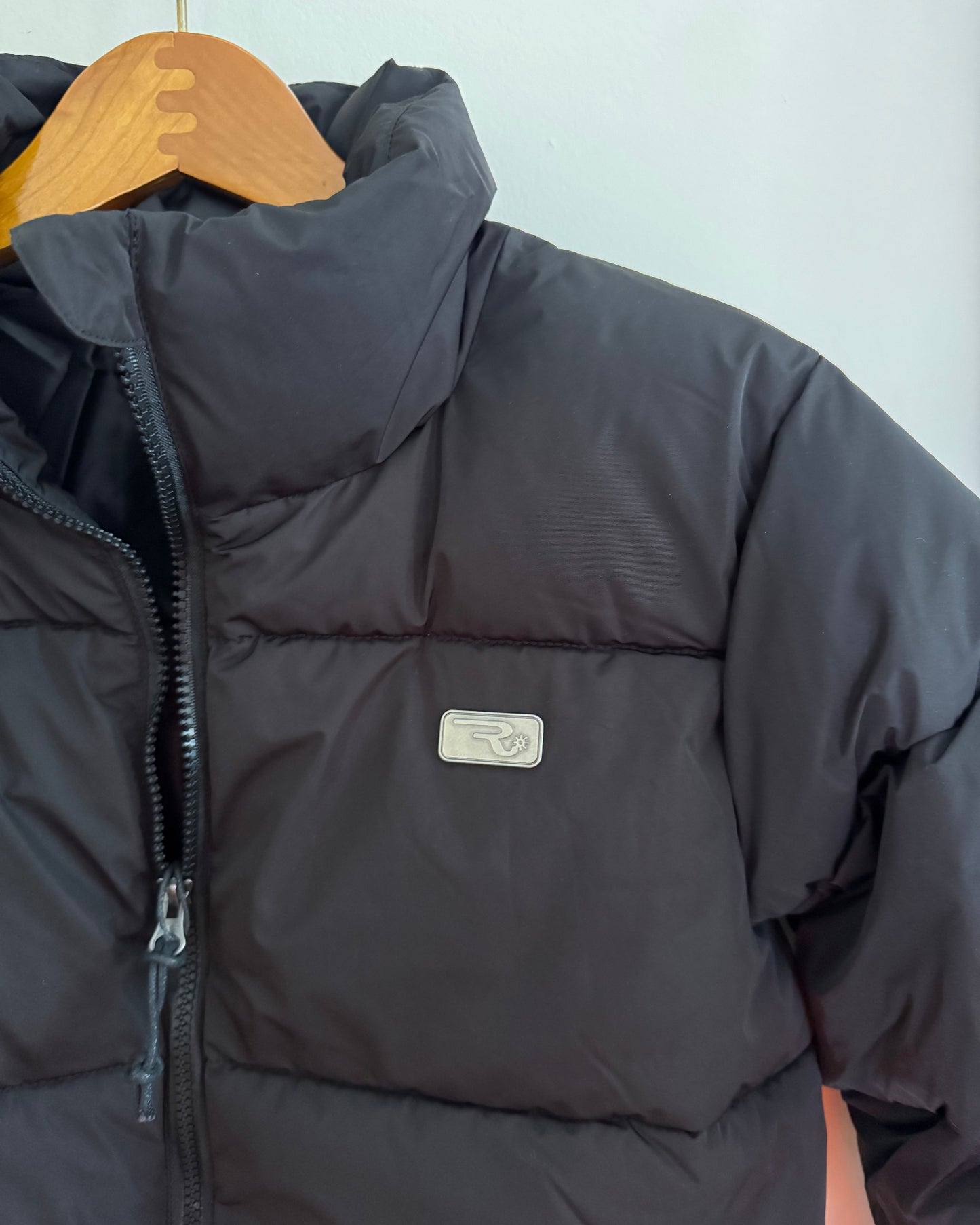 Close-up of a dark puffer jacket with a brand logo on a light background
