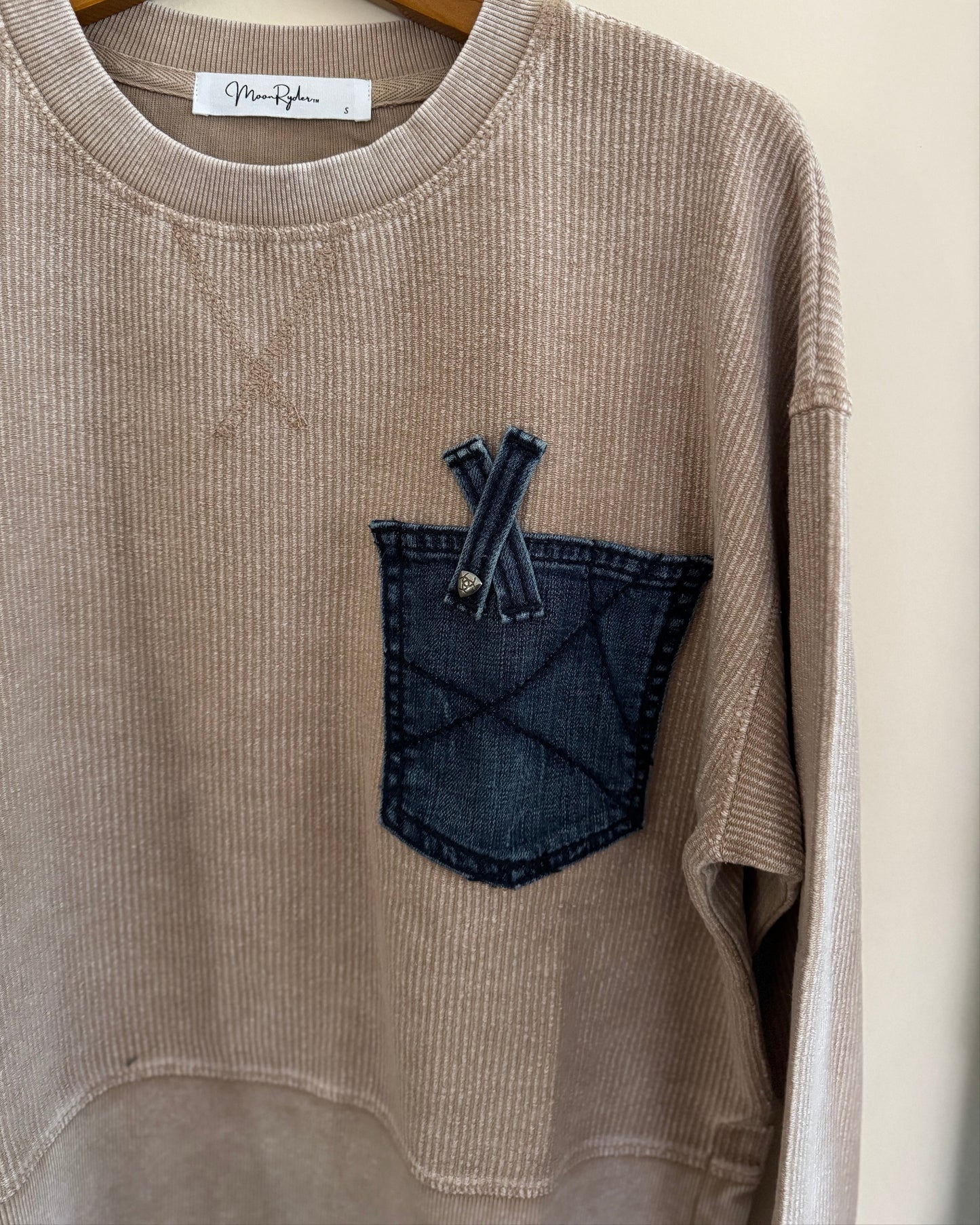 Beige sweatshirt with a denim pocket and hanger on a white background