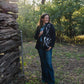 Woman standing in a forested area near a rustic wooden cabin.