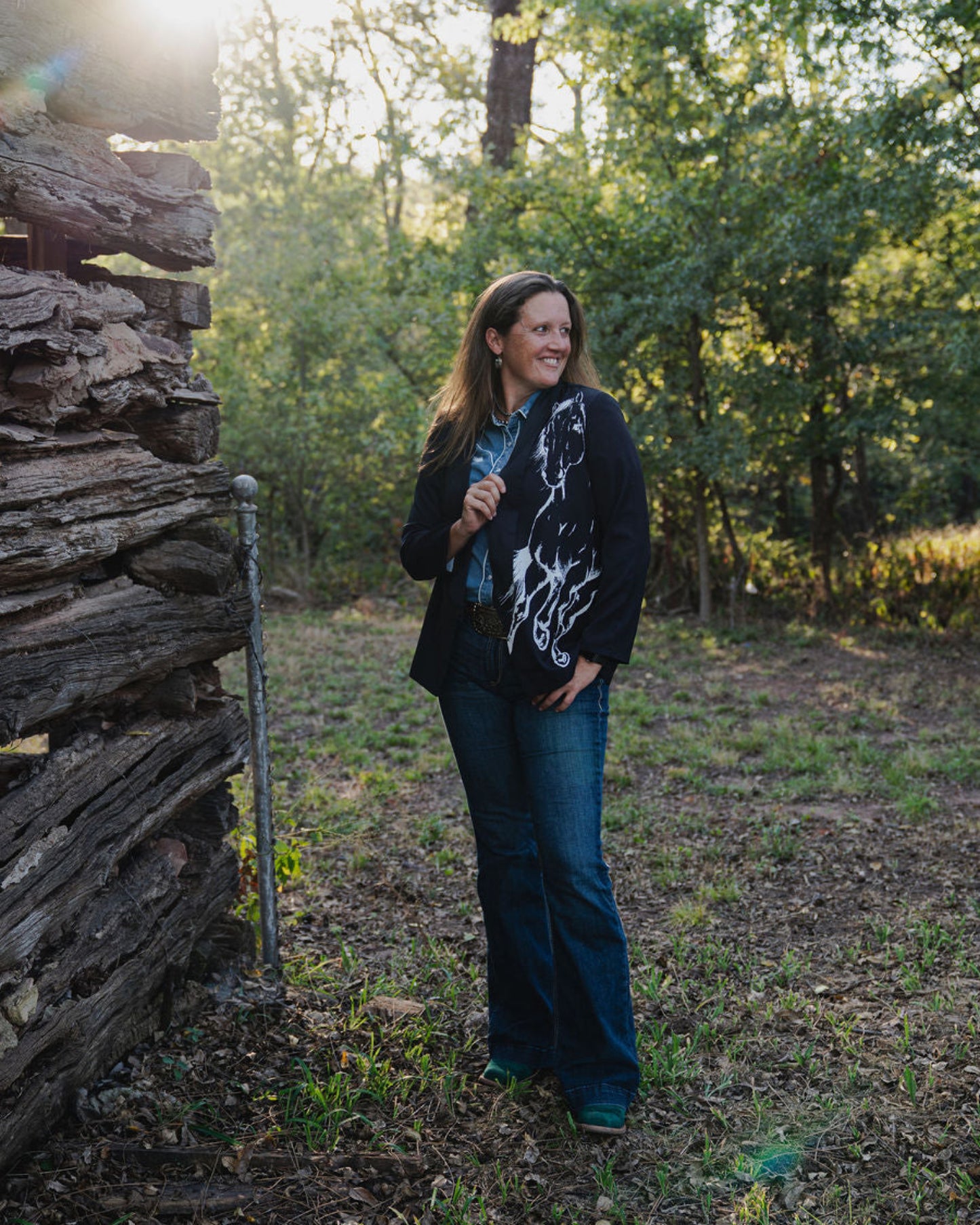 Woman standing in a forested area near a rustic wooden cabin.