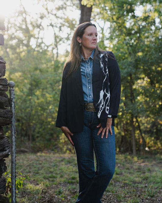 Woman standing outdoors in a natural setting with trees and sunlight filtering through.