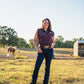 Woman standing in a field with a horse in the background