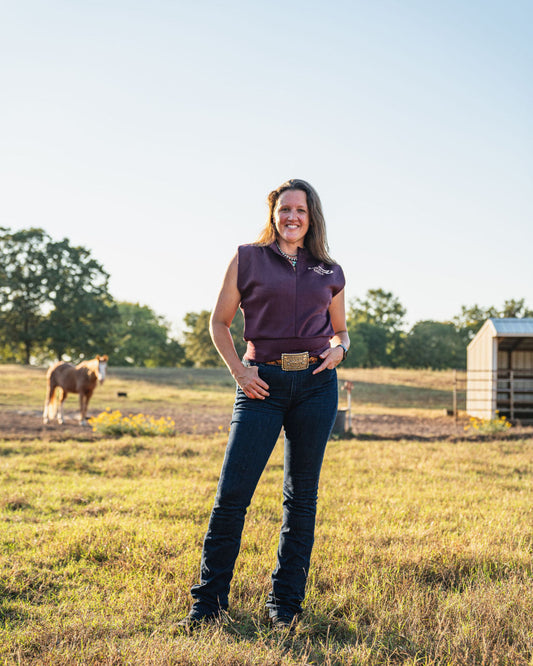 Woman standing in a field with a horse in the background