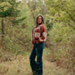 Woman wearing a patterned sweater and jeans standing in a forest