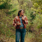 Woman wearing a patterned jacket and jeans standing in a forest