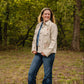 Woman standing in a forested area wearing a beige jacket with a floral design.