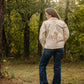 Person wearing a beige jacket with a design in a forest setting