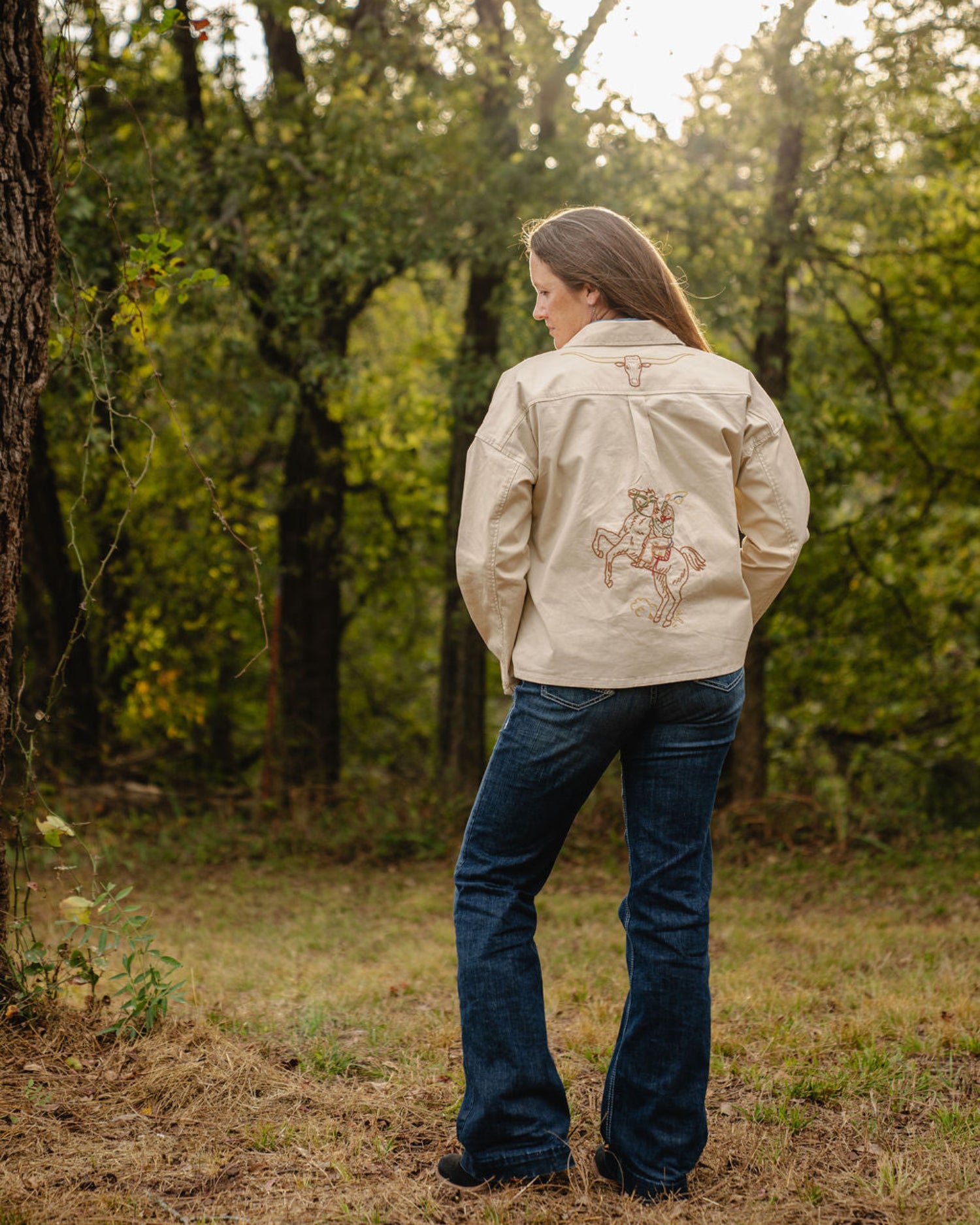 Person wearing a beige jacket with a design in a forest setting