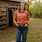 Woman standing in front of a log cabin in a natural setting