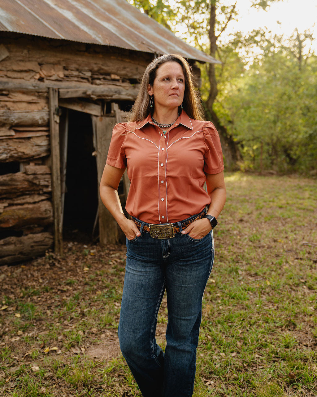 Woman standing in front of a log cabin in a natural setting