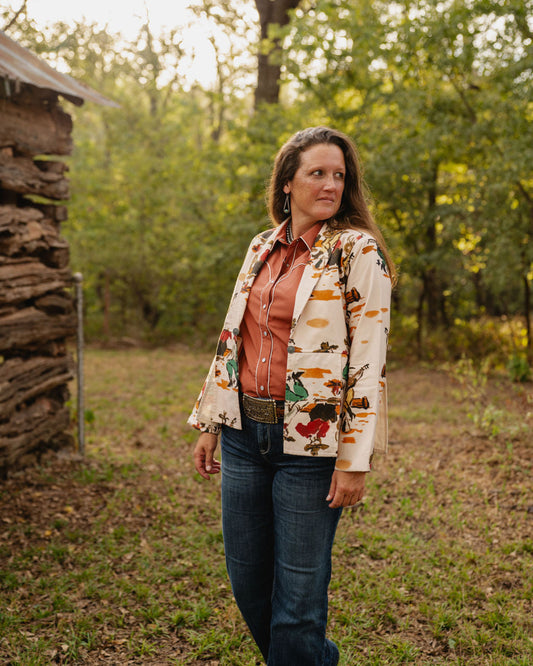 Woman standing outdoors in a natural setting with trees and a wooden structure.