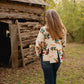 woman walking away wearing jeans and a jacket towards a rustic wooden building with trees in background