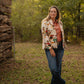 Woman standing outdoors in a natural setting wearing a floral jacket.