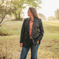 Woman standing in a field wearing a dark jacket and jeans.