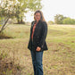 Woman standing in a field wearing a dark coat and blue jeans.