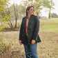 Woman standing in a field wearing a dark coat and jeans.
