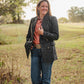 Woman standing in a field wearing a dark jacket and jeans.