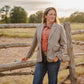 Woman standing in a field with a wooden fence and trees in the background