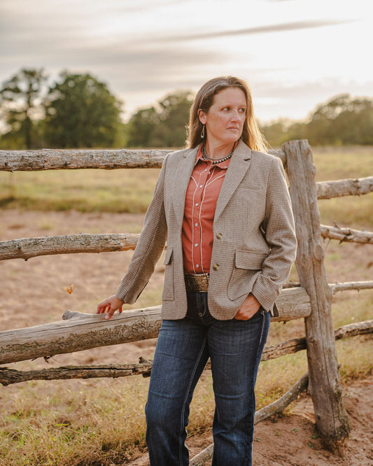 Woman standing in a field with a wooden fence and trees in the background