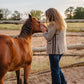 Woman petting a horse in an outdoor setting with a wooden fence and trees in the background.