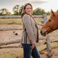 Woman standing next to a horse in an outdoor setting with a wooden fence and open field.