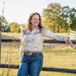 woman standing in front of a fence wearing a long sleeved shirt and jeans 