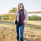 Woman standing in a field wearing a purple vest and jeans.