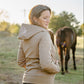 Woman in a beige jacket standing next to a horse in an outdoor setting