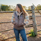 Woman standing in a field next to a wooden fence wearing a jacket with a logo.
