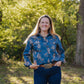 Woman wearing a blue floral shirt and jeans standing in a park with trees in the background
