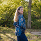 Woman wearing a blue floral jacket and dark pants standing in a park with trees in the background