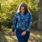 Woman wearing a blue floral shirt and jeans standing in a forested area