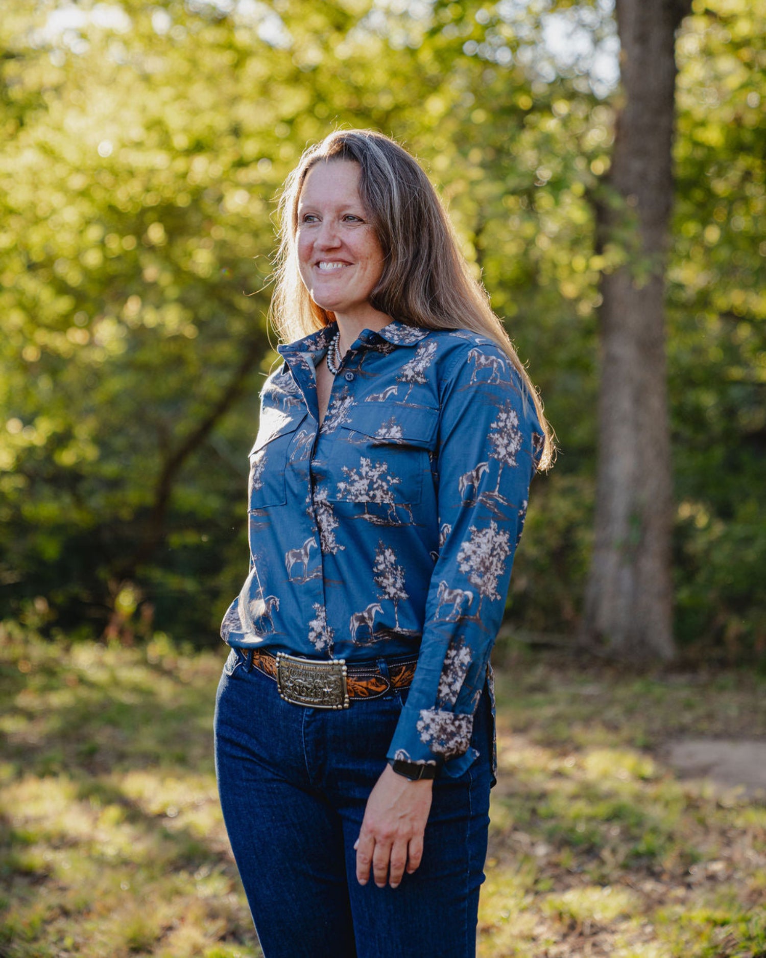 Woman wearing a blue floral shirt standing outdoors with greenery in the background