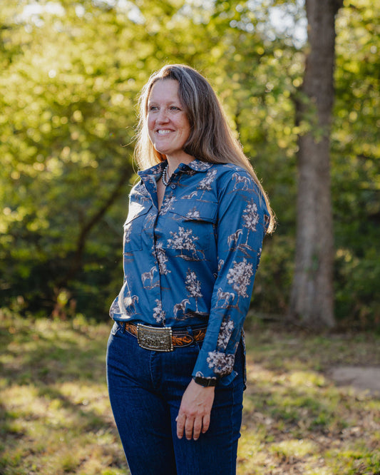 Woman wearing a blue floral shirt standing outdoors with greenery in the background