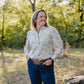 Woman standing outdoors in a natural setting with trees and greenery.