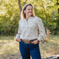 Woman standing outdoors in a natural setting with trees and greenery.