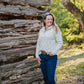 Woman standing in front of a rustic wooden cabin in a natural setting