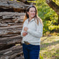Woman standing in front of a wooden structure with trees in the background