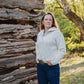 Woman standing in front of a rustic wooden cabin with trees in the background