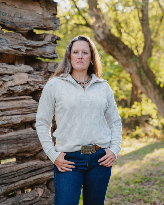 Woman standing in a natural setting with trees and wooden logs.