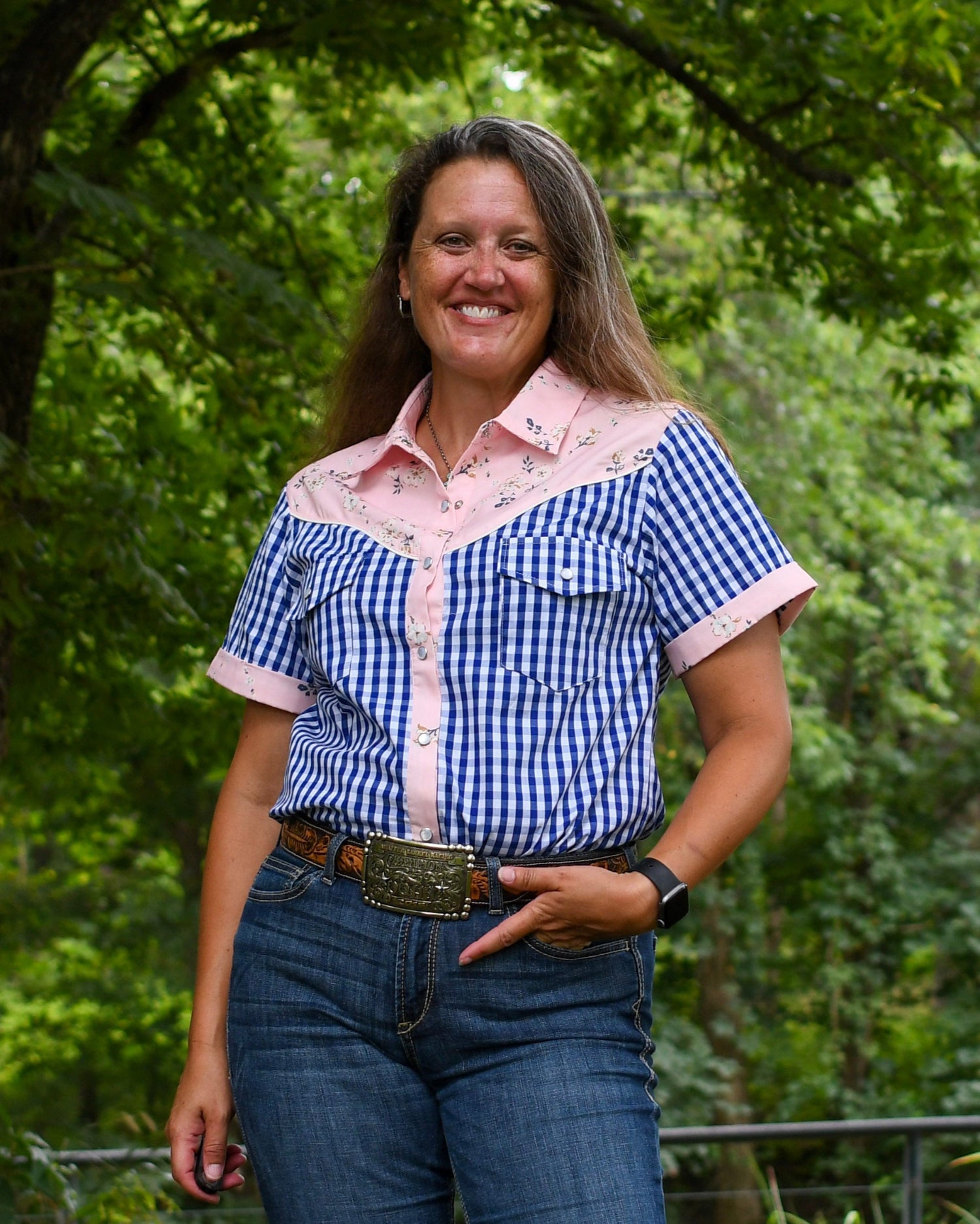 Woman wearing a blue checkered shirt with pink accents outdoors