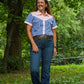 Woman wearing a blue checkered shirt and jeans standing in a forested area