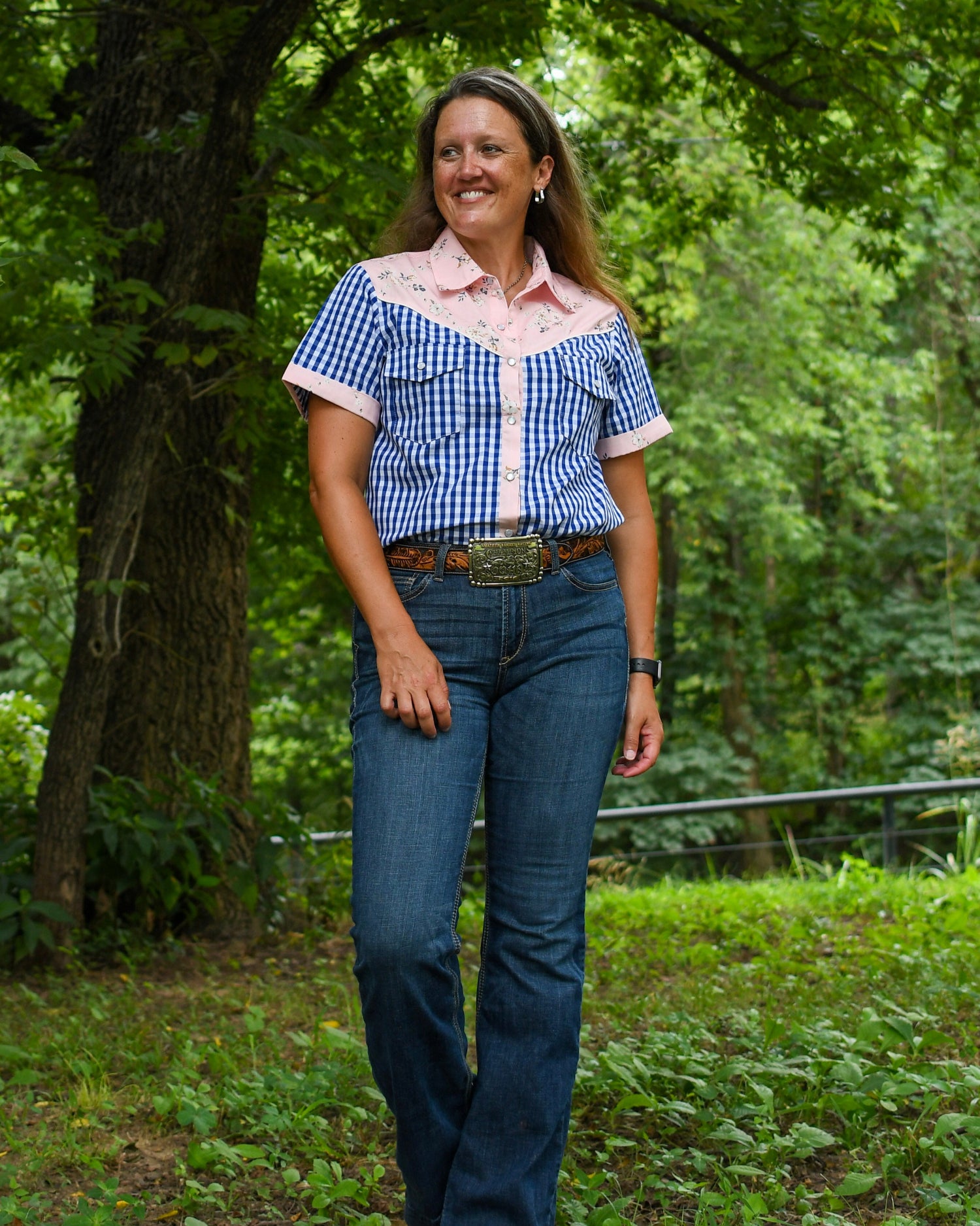 Woman wearing a blue checkered shirt and jeans standing in a forested area