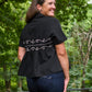 Woman wearing a black blouse with white embroidery in a forest setting