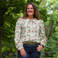 Woman wearing a patterned blouse and jeans standing in a forested area