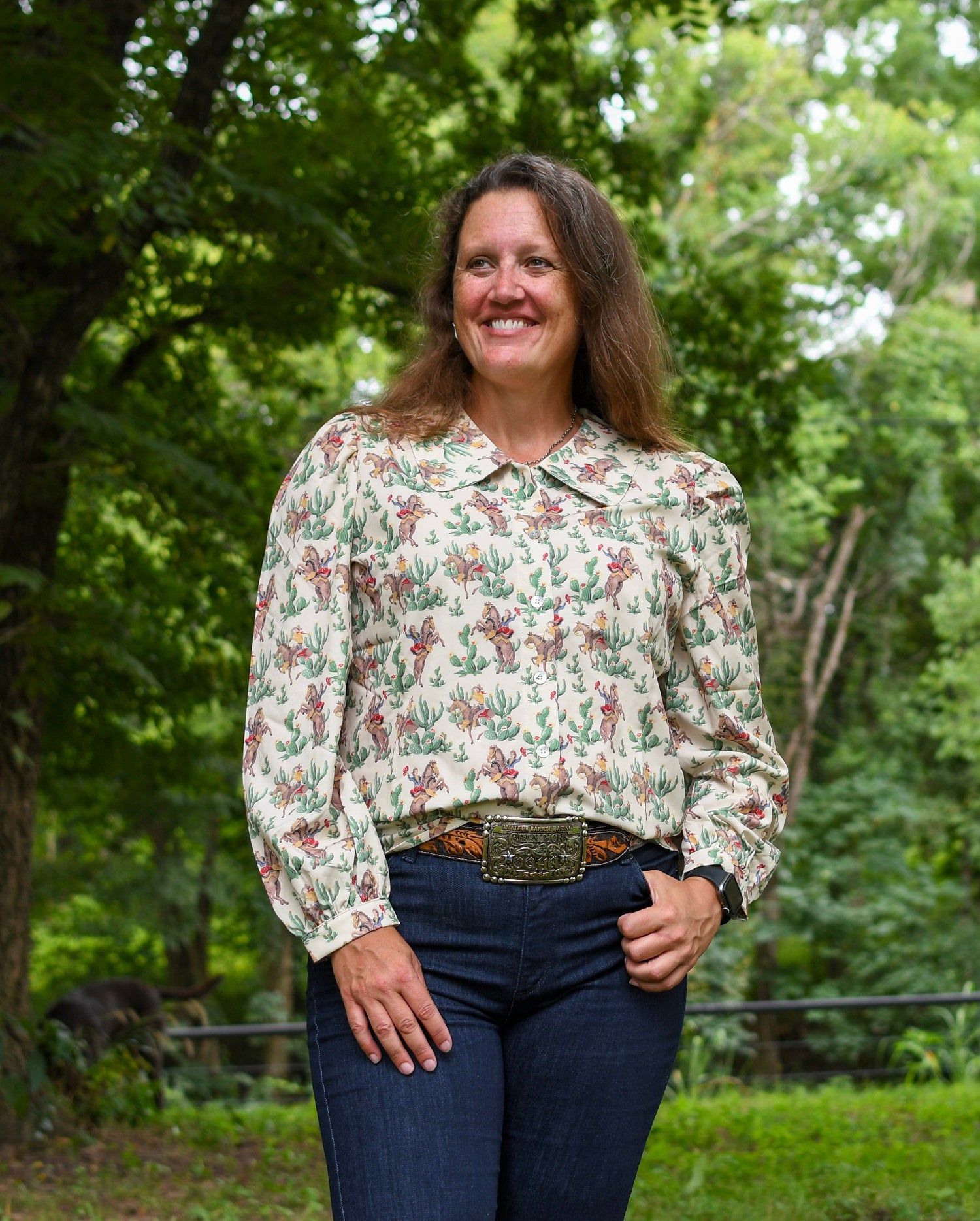 Woman wearing a patterned blouse and jeans standing in a forested area