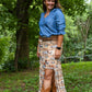 Woman in a blue shirt and patterned skirt standing in a forested area