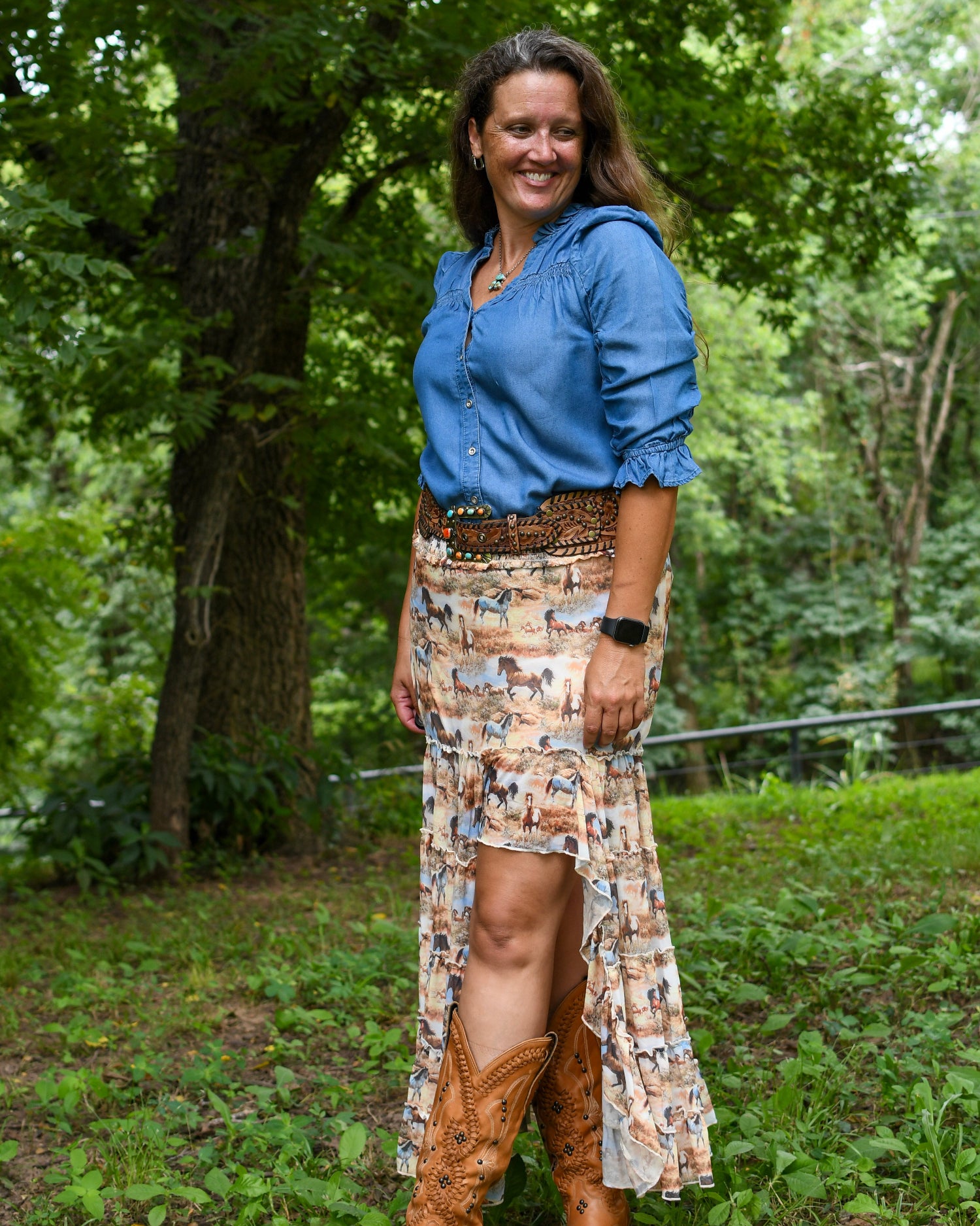Woman in a blue shirt and patterned skirt standing in a forested area