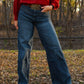 woman standing in trees wearing jeans and a sweater