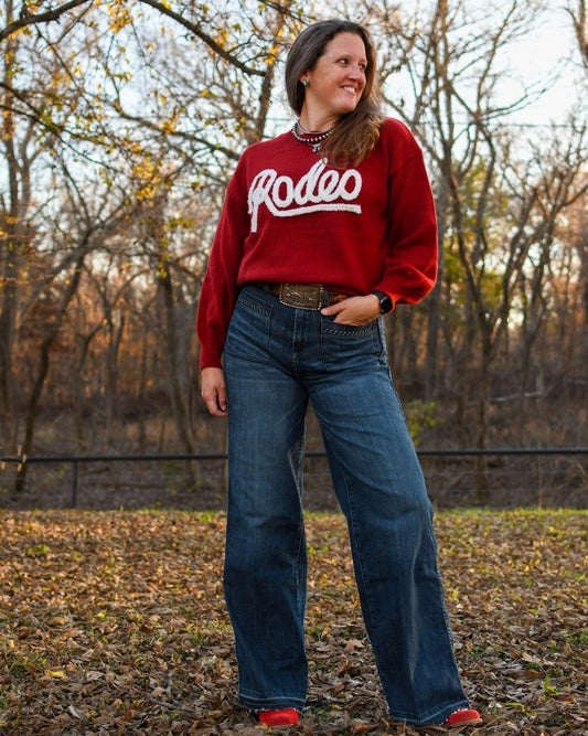 Model standing in leaves wearing a rodeo sweater and jeans